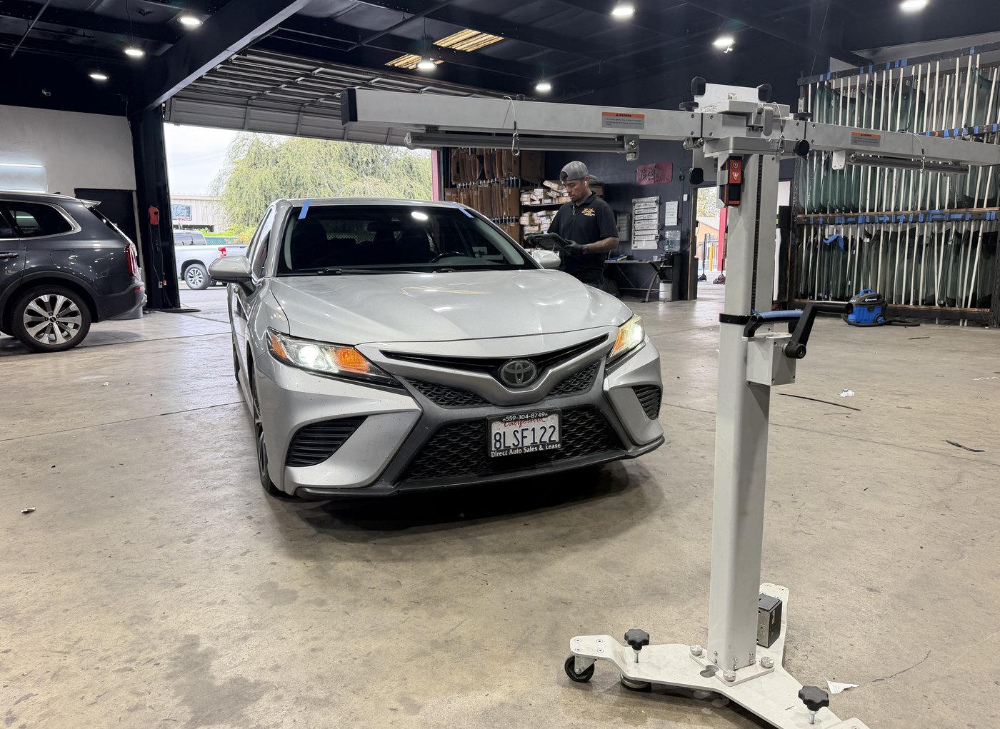 An ADAS calibration rig set up in front of a vehicle in the Best Auto Care shop, with the glass inventory rack behind it