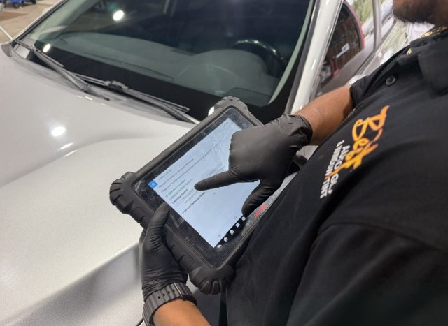 A Best Auto Care technician documenting calibration work on a rugged tablet against a windshield