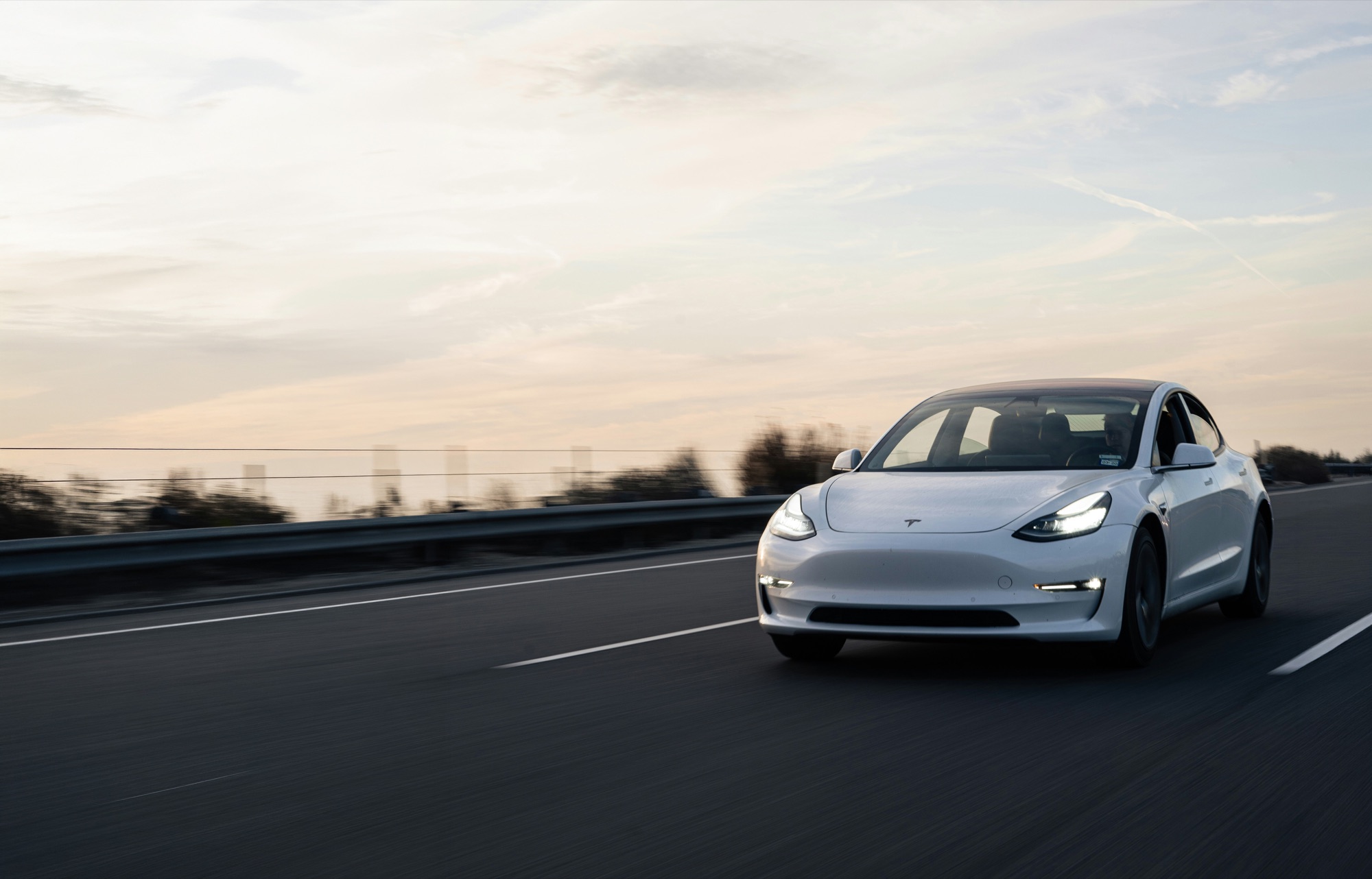 A white Tesla Model 3 on the highway at dusk