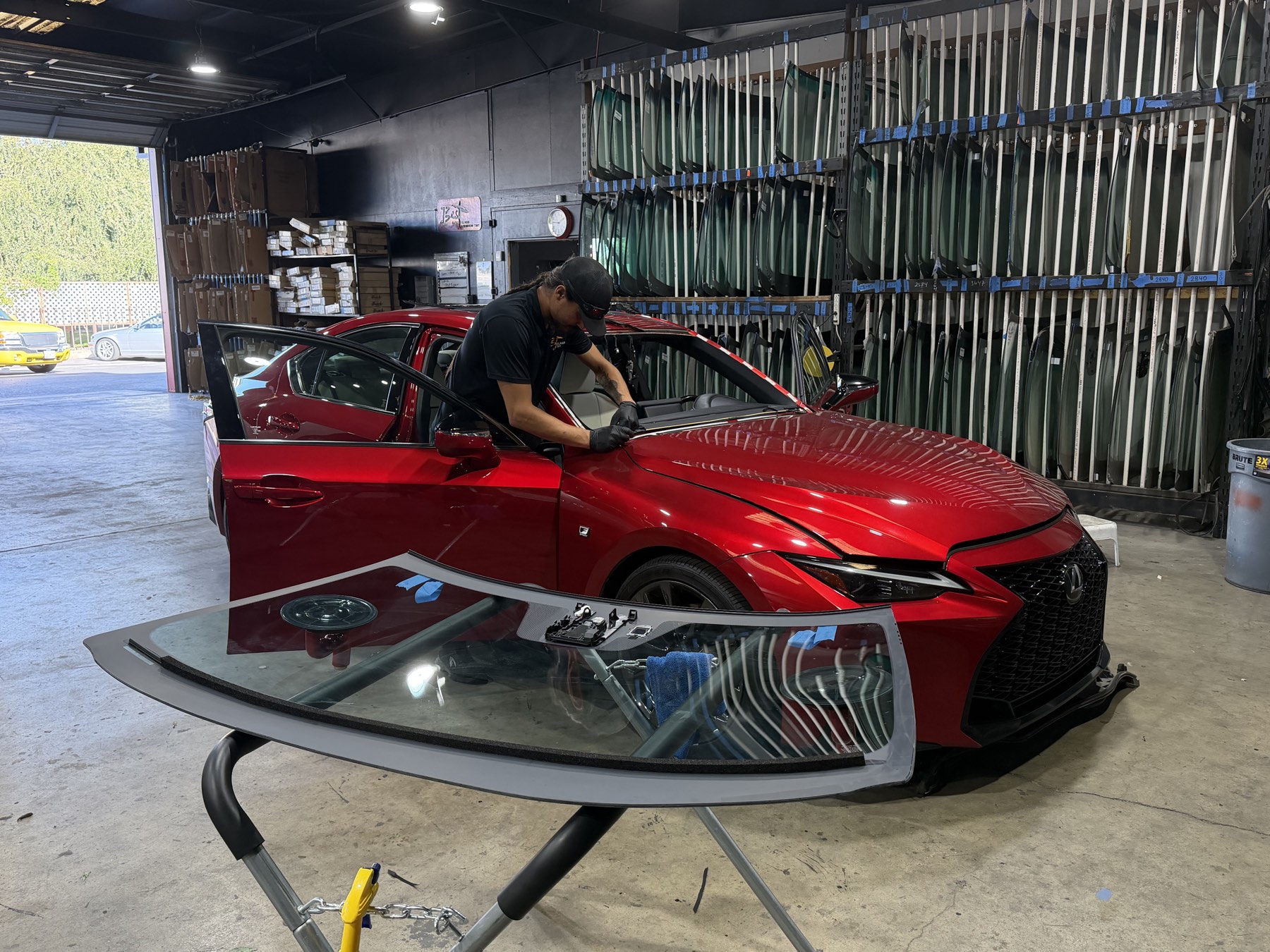 A technician replacing a windshield at Best Auto Care, with the shop's full glass inventory racked behind him